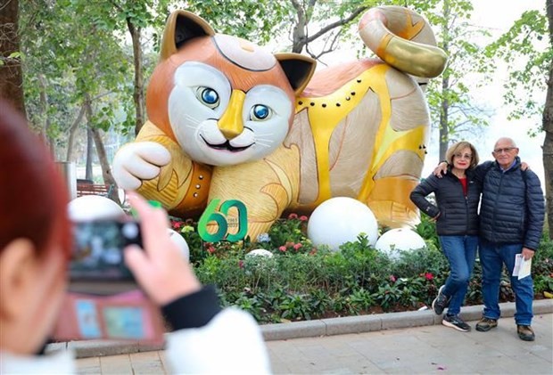 Foreign tourists pose for a photo besides a statue of the cat, the symbol of Lunar New Year 2023, in Hanoi. (Photo: VNA)