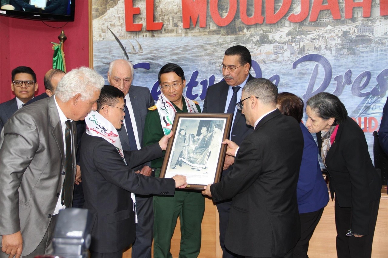Vietnamese Ambassador to Algeria Tran Quoc Khanh (second from left) presents to General Director of El Moudjahid Brahim Takheroubt with a photo of General Vo Nguyen Giap handing over a Vietnamese flag to the Algerian Defence Minister on the occasion of hi