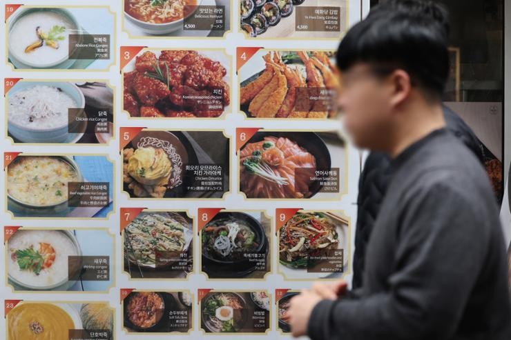 People walk past a restaurant's menu board on a street in Myeong-dong, Seoul, April 3. Yonhap