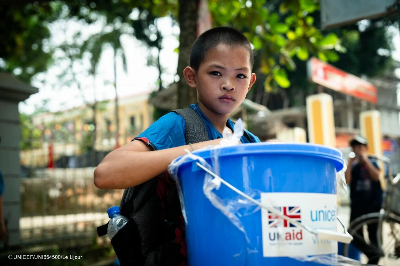 A child holds a UNICEF-supplied Child Protection Kit, containing essential items for hygine and safety needs (toothbrush, toothpaste, soap, toilet paper, sanitary napkins, raincoat, mosquito net, boots) as well as leaflets for parents and children for protection and psychosocial care. (Photo: UNICEF)