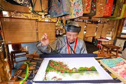 An artisan embroiders a painting at the exhibition area. (Photo: VNA)