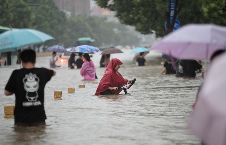 Người dân lội qua dòng nước lũ trên con đường ngập lụt trong bối cảnh mưa lớn ở Trịnh Châu, tỉnh Hà Nam, ngày 20 tháng 7. China Daily qua REUTERS